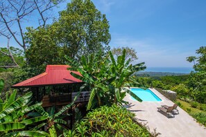 A secluded villa with a red-roofed structure, a swimming pool, and lush greenery.