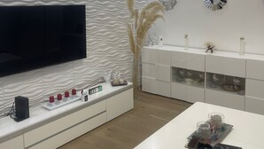 A modern living room with a flat-screen TV, white entertainment unit, decorative wall clocks, and a wooden floor. - Modern apartment/city center near (Wien)