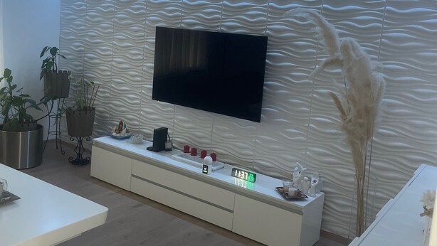 A modern living room with a flat-screen TV mounted on a textured wall, a white console table with a clock and decorative items, and a wooden floor. - Modern apartment/city center near (Wien)