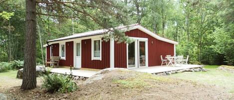 Eine rote Holzhütte mit Veranda und Essbereich, im Vordergrund ein großer Fels.