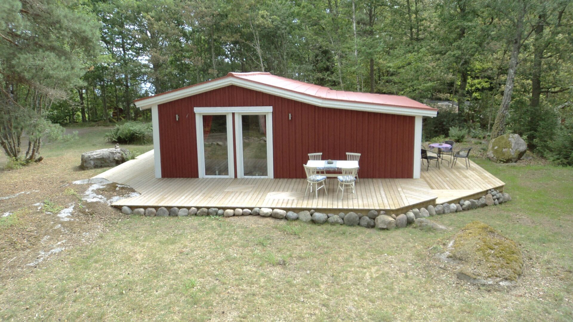 A wooden deck with a red building, a glass door, and a table with chairs.