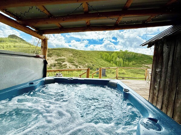 Un bain à remous avec une terrasse en bois et une vue sur des collines verdoyantes.