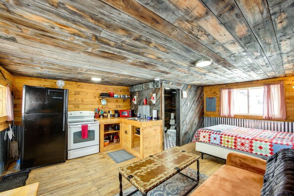 Ein rustikales Blockhaus-Interieur mit Küchenzeile, Holzwänden, einem Bett und einer Bank.