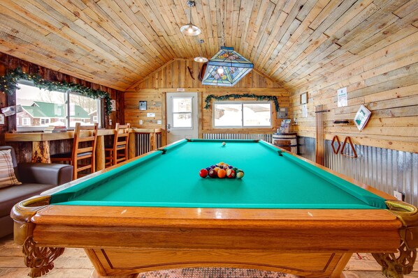 Une table de billard dans une pièce en bois, avec un plafond haut et une vue sur les maisons à l’extérieur.
