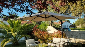 An outdoor patio with a table and chairs, a covered seating area, and a view of a house in the background. - La Baule beach 1.5 km away. Bright house sleeps 9, enclosed garden  (Guérande)