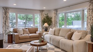 A spacious living room with two sofas, a coffee table, and large windows offering a view of the outdoors.