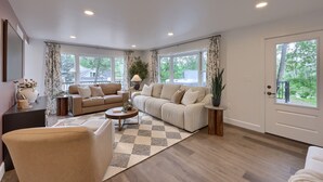 A spacious living room with a large sofa, a coffee table, and a view of the outdoors through large windows.