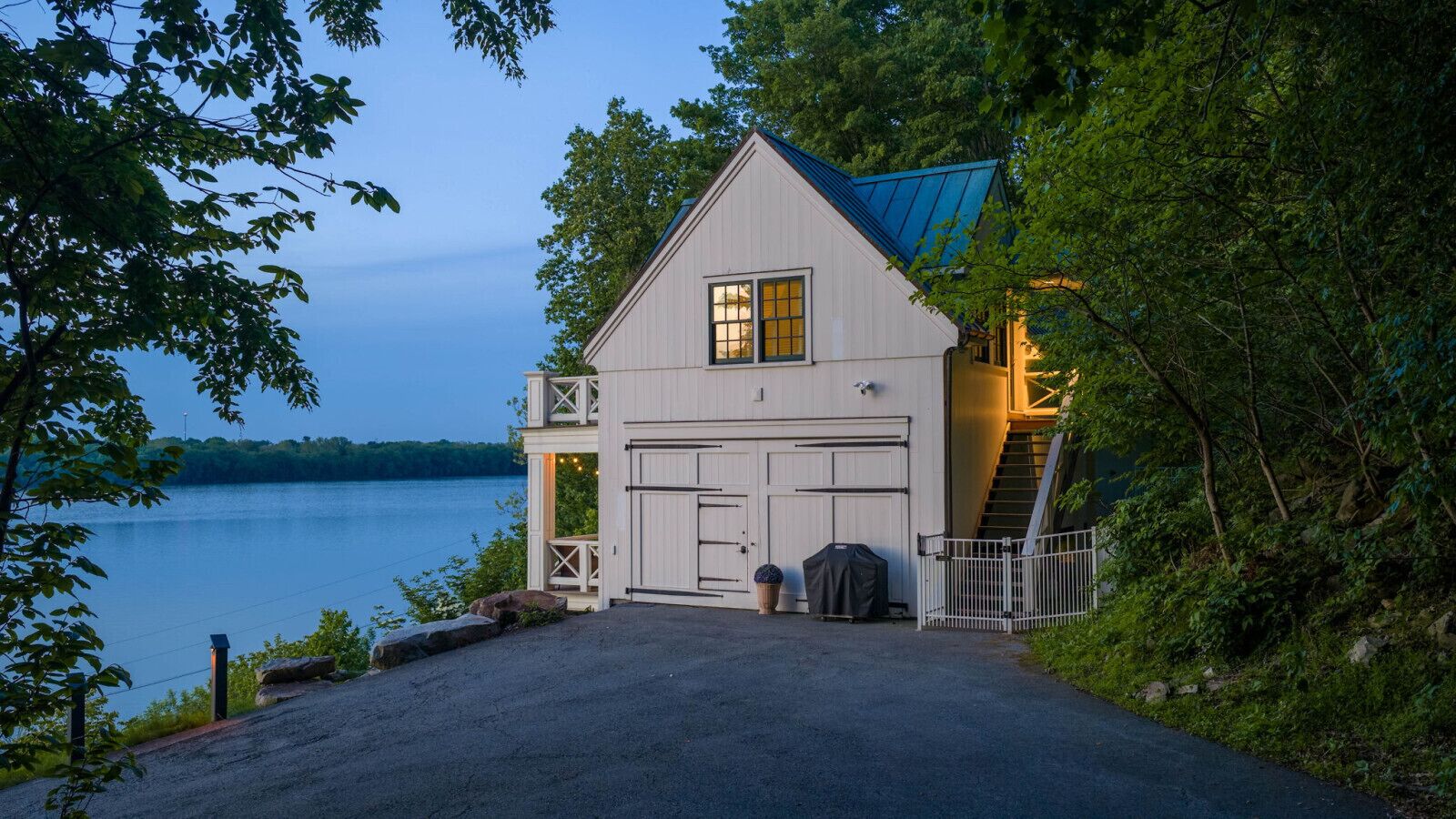 A lakeside house with a garage, a covered porch, and a staircase leading to the entrance.