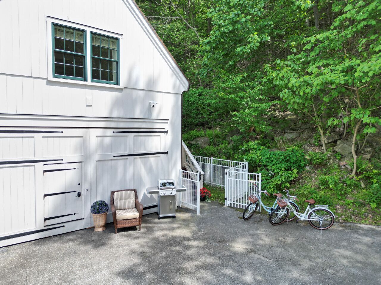 A white house with a garage, a staircase leading to a porch, a chair, a small table, and two bicycles.