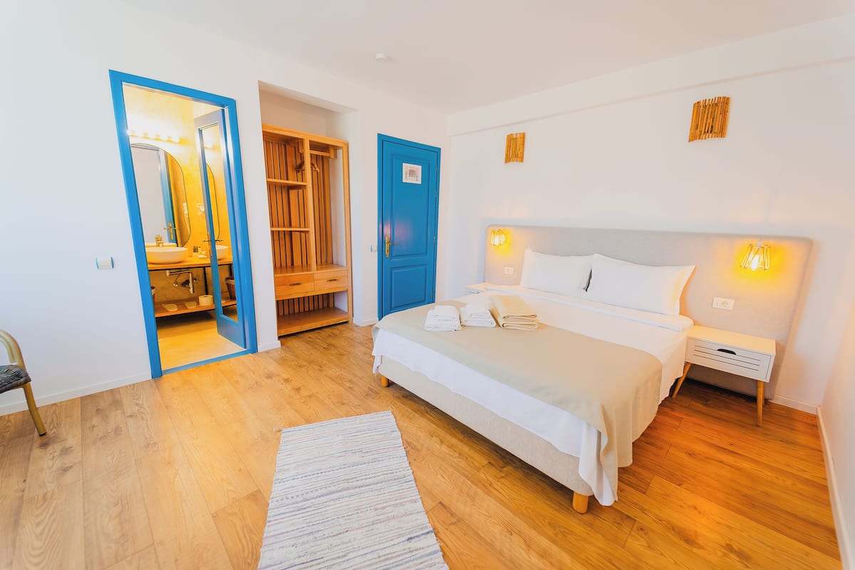 A bedroom with a bed, bedside tables, a nightstand, a mirror, a wardrobe, and a door.