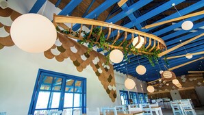L’intérieur d’un restaurant présente des poutres bleues au plafond, des luminaires sphériques suspendus et une structure en bois aux lignes courbes agrémentée de verdure.