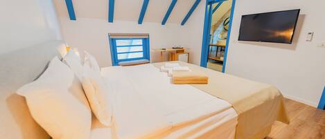 A bedroom with a bed, a desk, a TV, and a window.