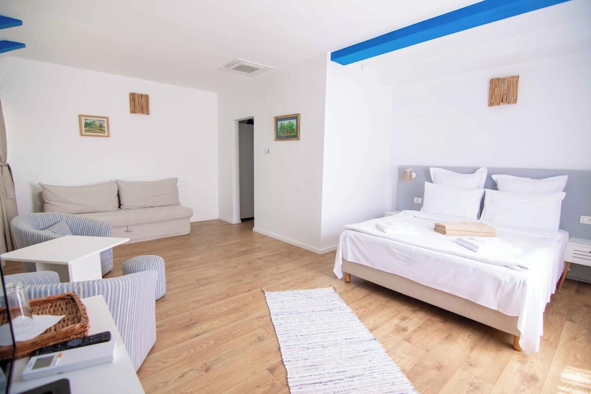 A modern hotel room with a bed, a sofa, a small table, and a wooden floor.