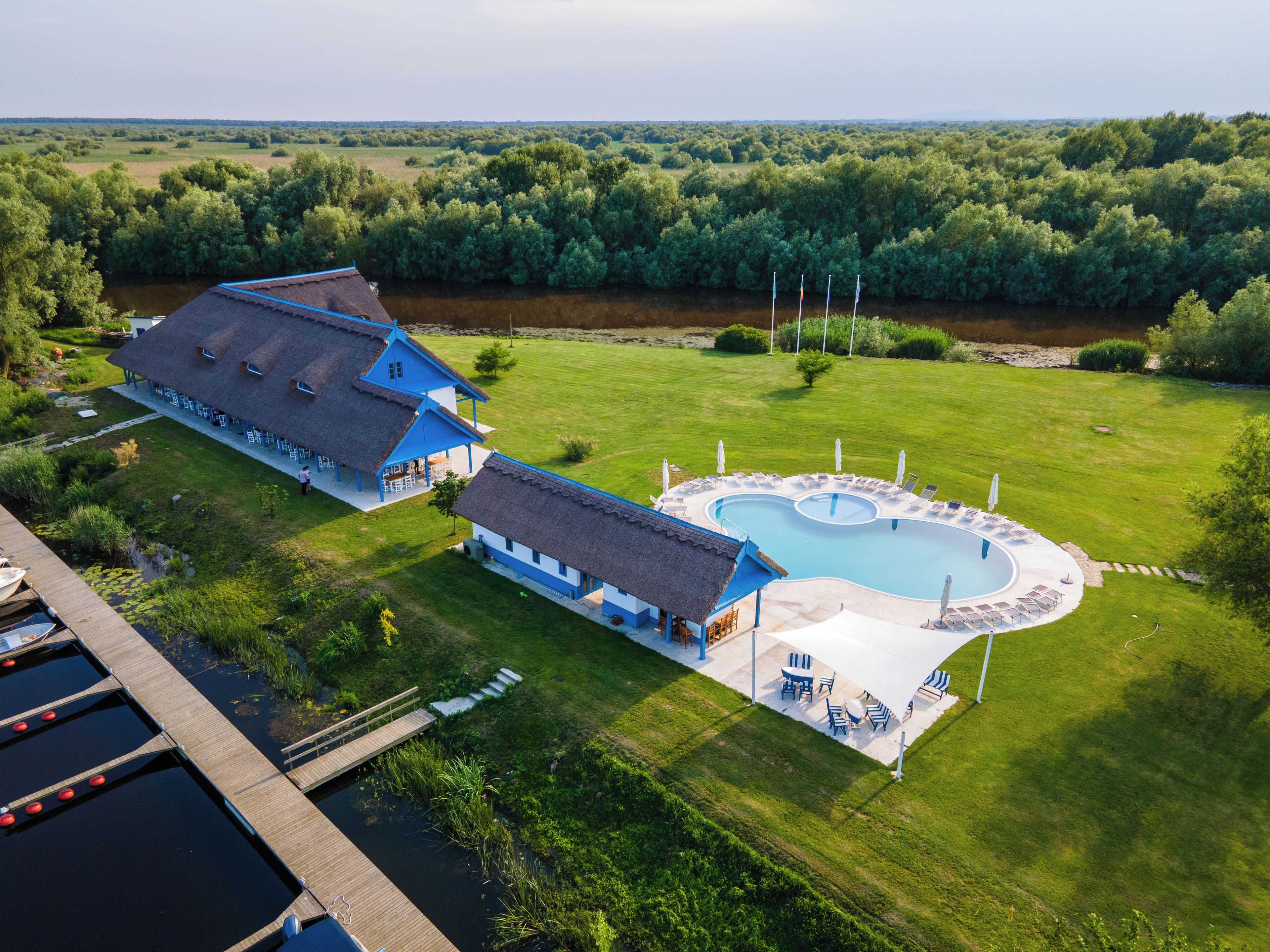 Vista aérea de una propiedad con piscina, terraza de madera y una casa grande con techo azul.