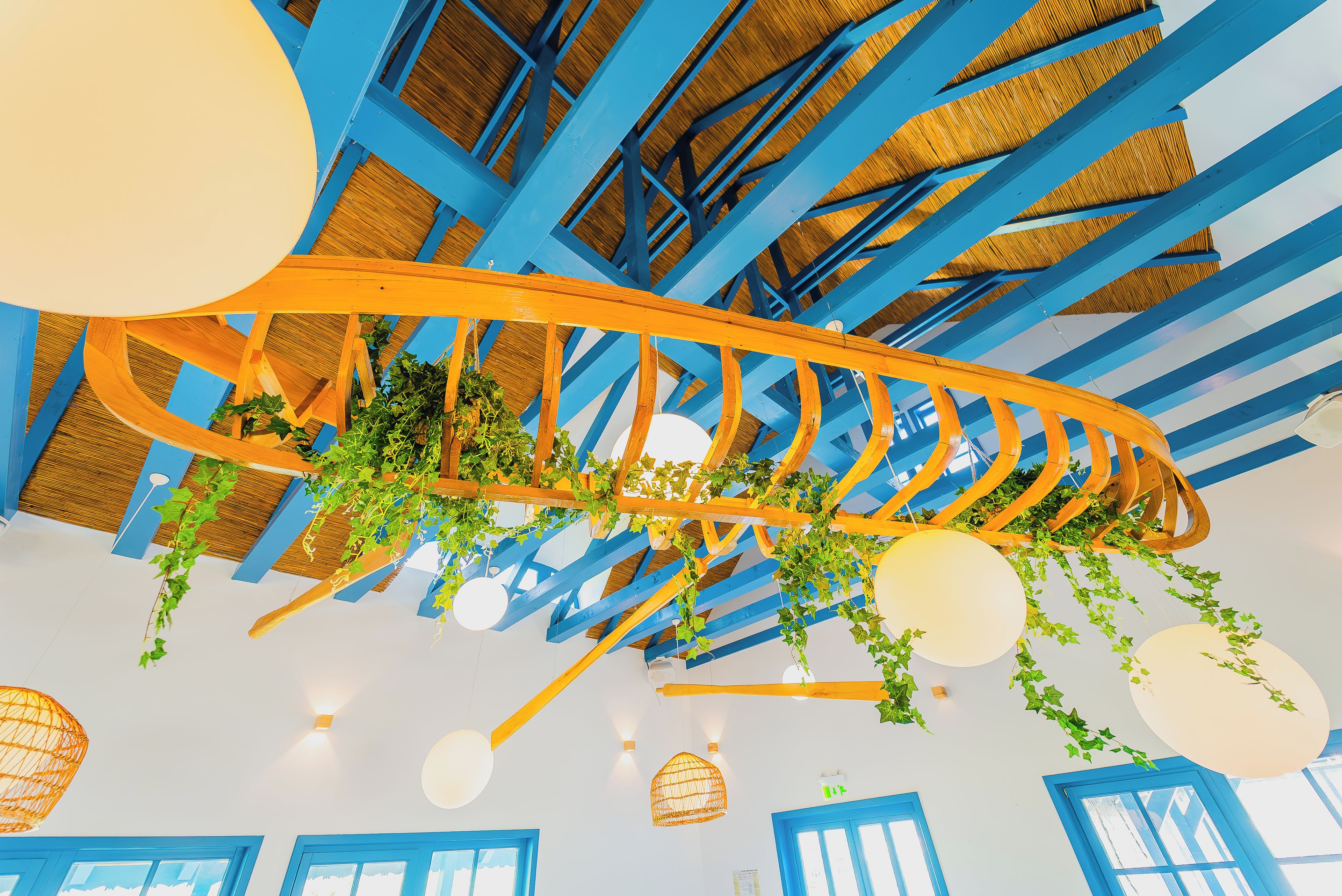 Un plafond avec des poutres bleues, des plantes suspendues et des luminaires sphériques.