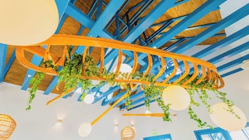 Un plafond avec des poutres bleues, des plantes suspendues et des luminaires sphériques.