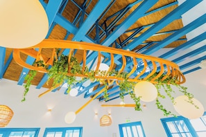 Un techo con vigas azules, plantas colgantes e lámparas esféricas.