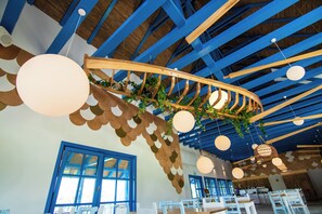 A restaurant interior with blue ceiling beams, hanging spherical lights, and a wooden curved structure with greenery.