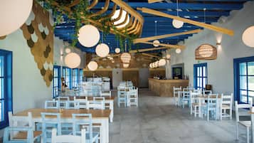 Un vaste espace dédié à la salle à manger, avec des tables et des chaises blanches, un plafond en bois et des lampes sphériques suspendues.