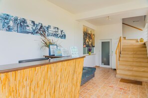 A reception area with a wooden reception desk, a large blue and white painting, a black leather sofa, and a staircase.
