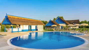 Une piscine avec un bâtiment à toit de chaume et un autre bâtiment avec un toit bleu.