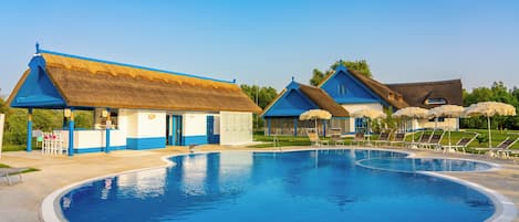 Une piscine avec un bâtiment à toit de chaume et un autre bâtiment avec un toit bleu.
