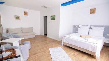 A modern hotel room with a bed, a sofa, a small table, and a wooden floor.