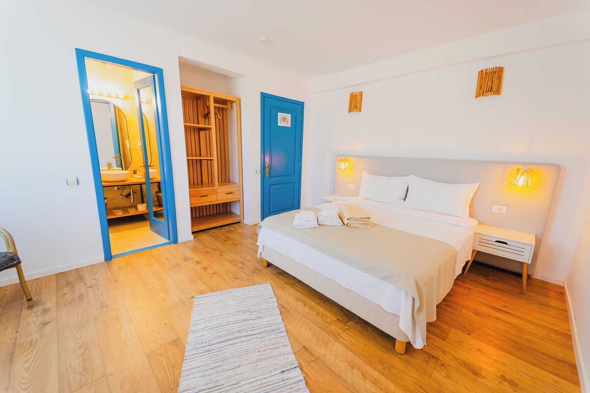 A bedroom with a bed, bedside tables, a nightstand, a mirror, a wardrobe, and a door.