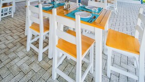 Un espace de restauration extérieur abrité, doté de tables en bois et de chaises blanches, offrant une vue sur le paysage environnant.