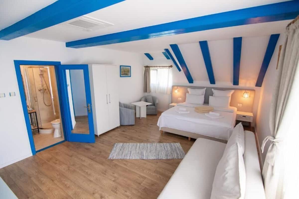 A bedroom with a wooden floor, a bed with white bedding, a nightstand, and a desk with a chair.