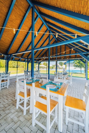 An outdoor covered dining area with wooden tables and white chairs, featuring a view of the surrounding landscape. - Cherhana Resort (Crisan)