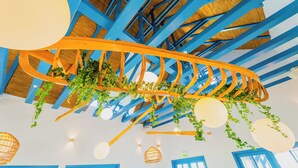 Un plafond avec des poutres bleues, des plantes suspendues et des luminaires sphériques.