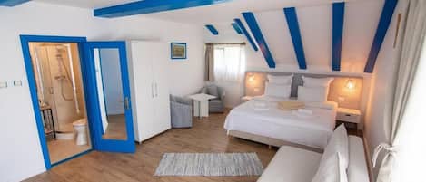 Un dormitorio con suelo de madera, una cama con ropa blanca, una mesita de noche y un escritorio con una silla.