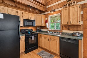 A kitchen with wooden cabinets, a black refrigerator, a stove, a microwave, a sink, and a dishwasher.