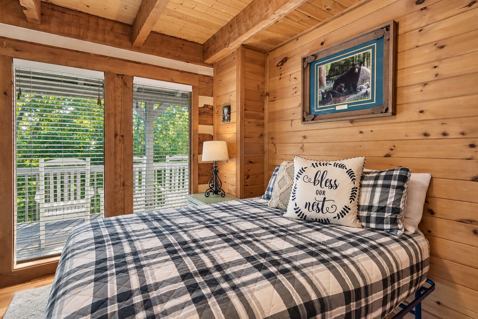 Quarto de cabana de madeira com uma cama, um quadro na parede e vista pela janela.