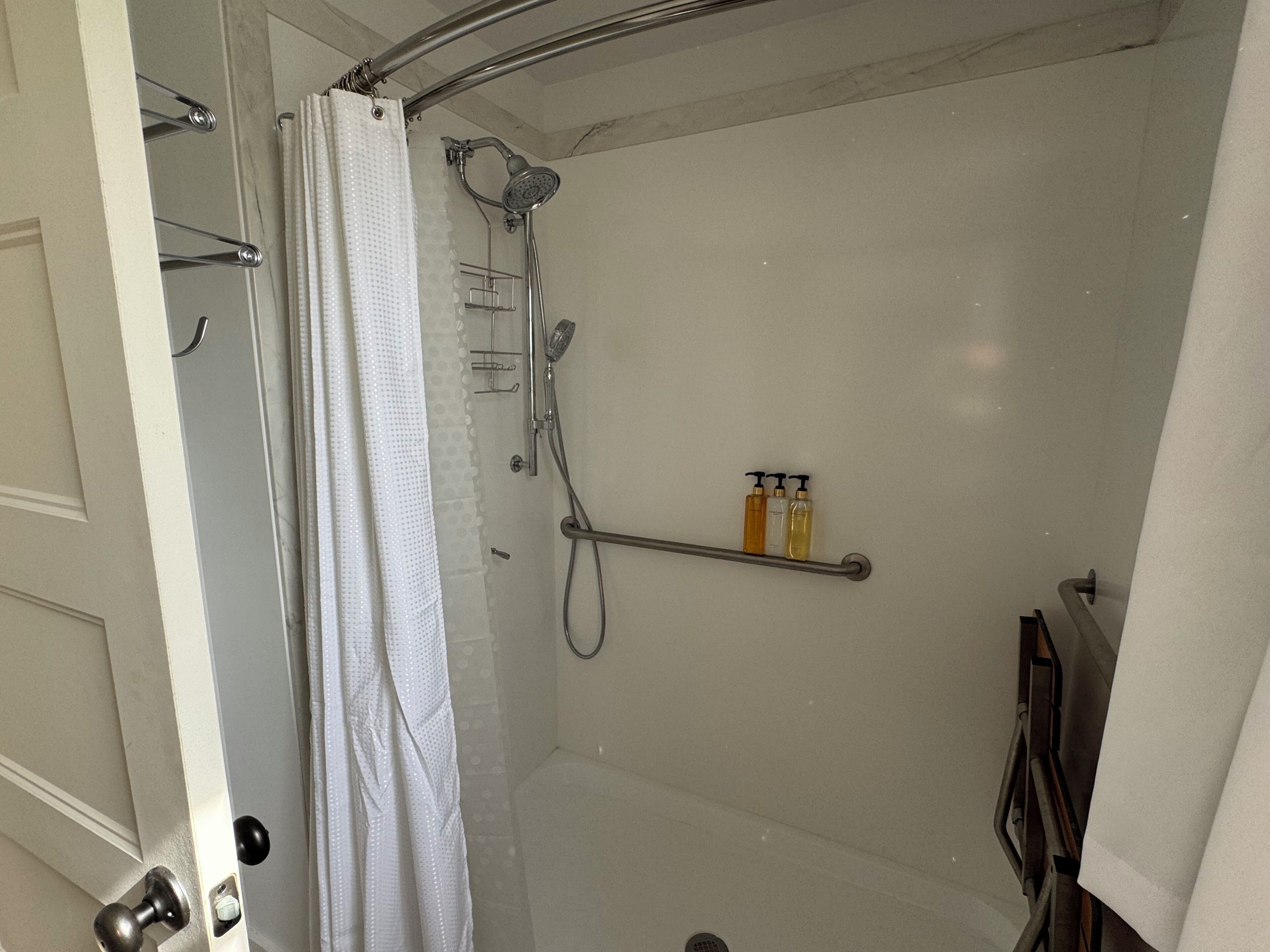 A shower area with a glass door, a showerhead, and a shelf with toiletries.