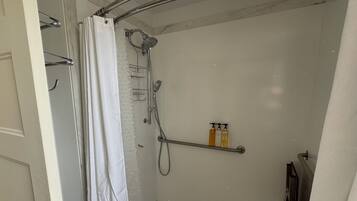 A shower area with a glass door, a showerhead, and a shelf with toiletries.