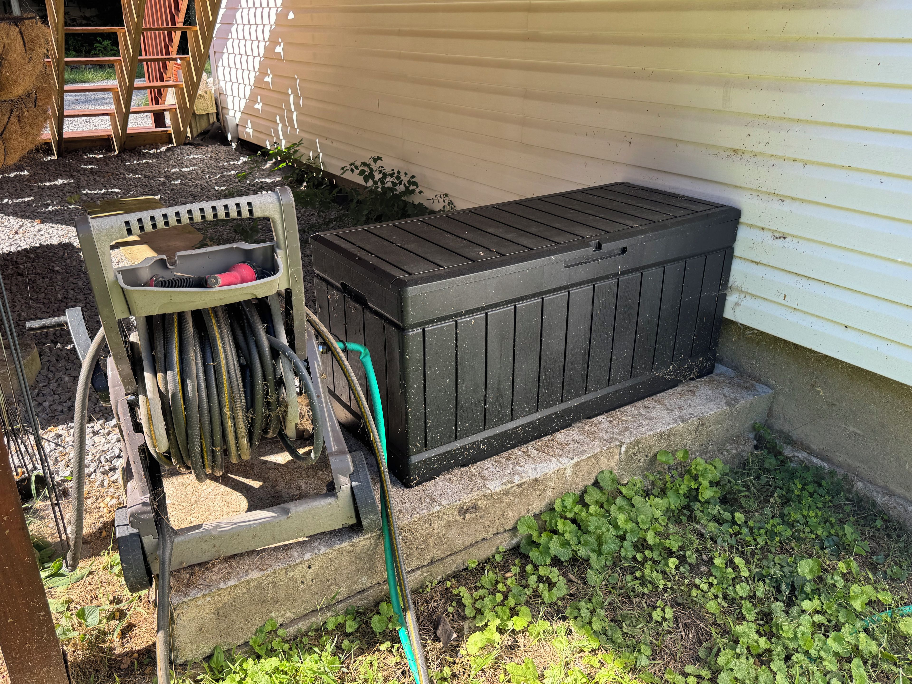 A utility box and a hose connected to it, placed on a concrete step next to a house.