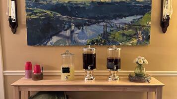 A room with a large landscape painting, a table with drink dispensers, a wicker basket, and a cooler.
