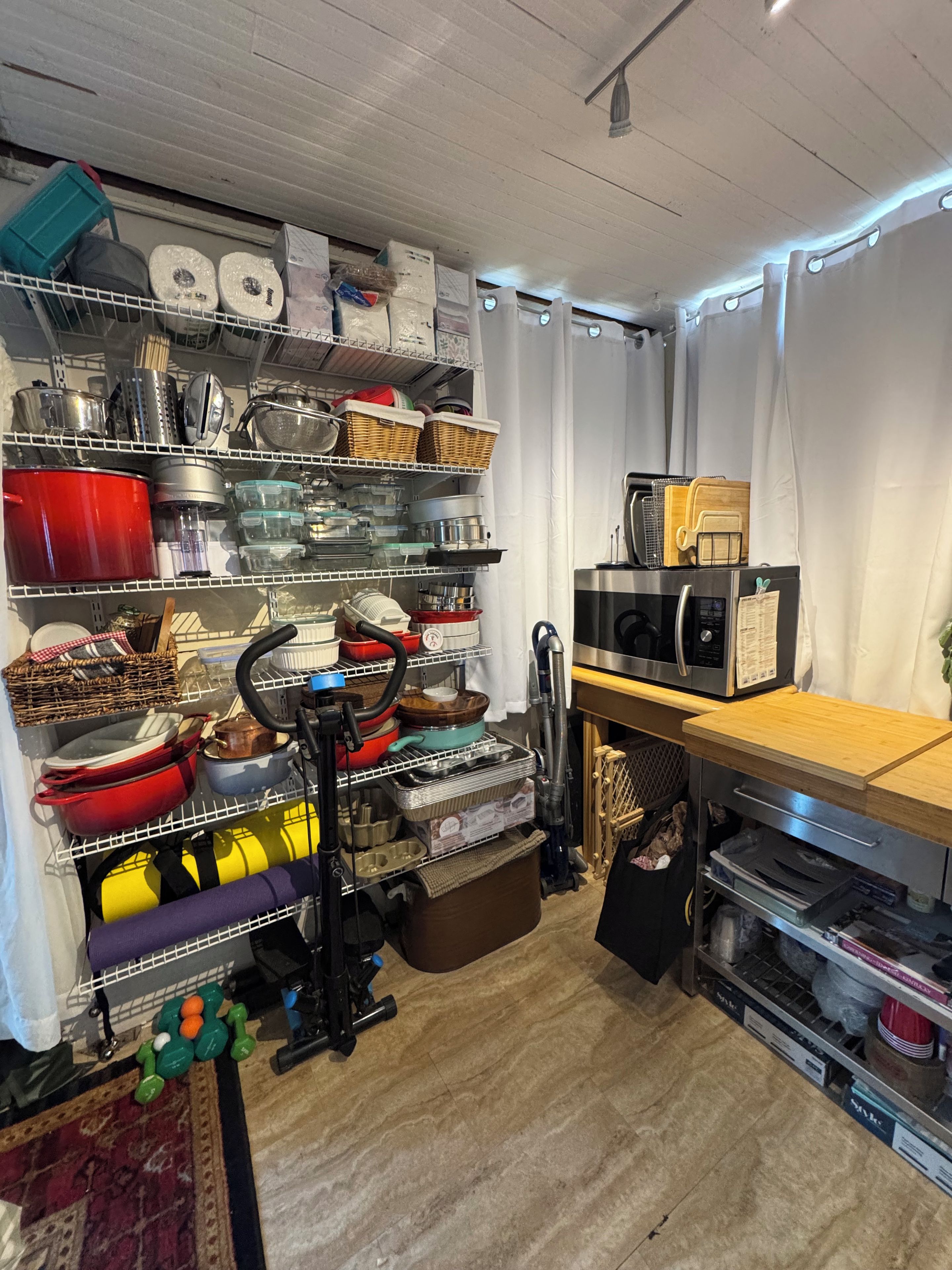 A kitchen with shelves stocked with cookware, a microwave, and a vacuum cleaner.