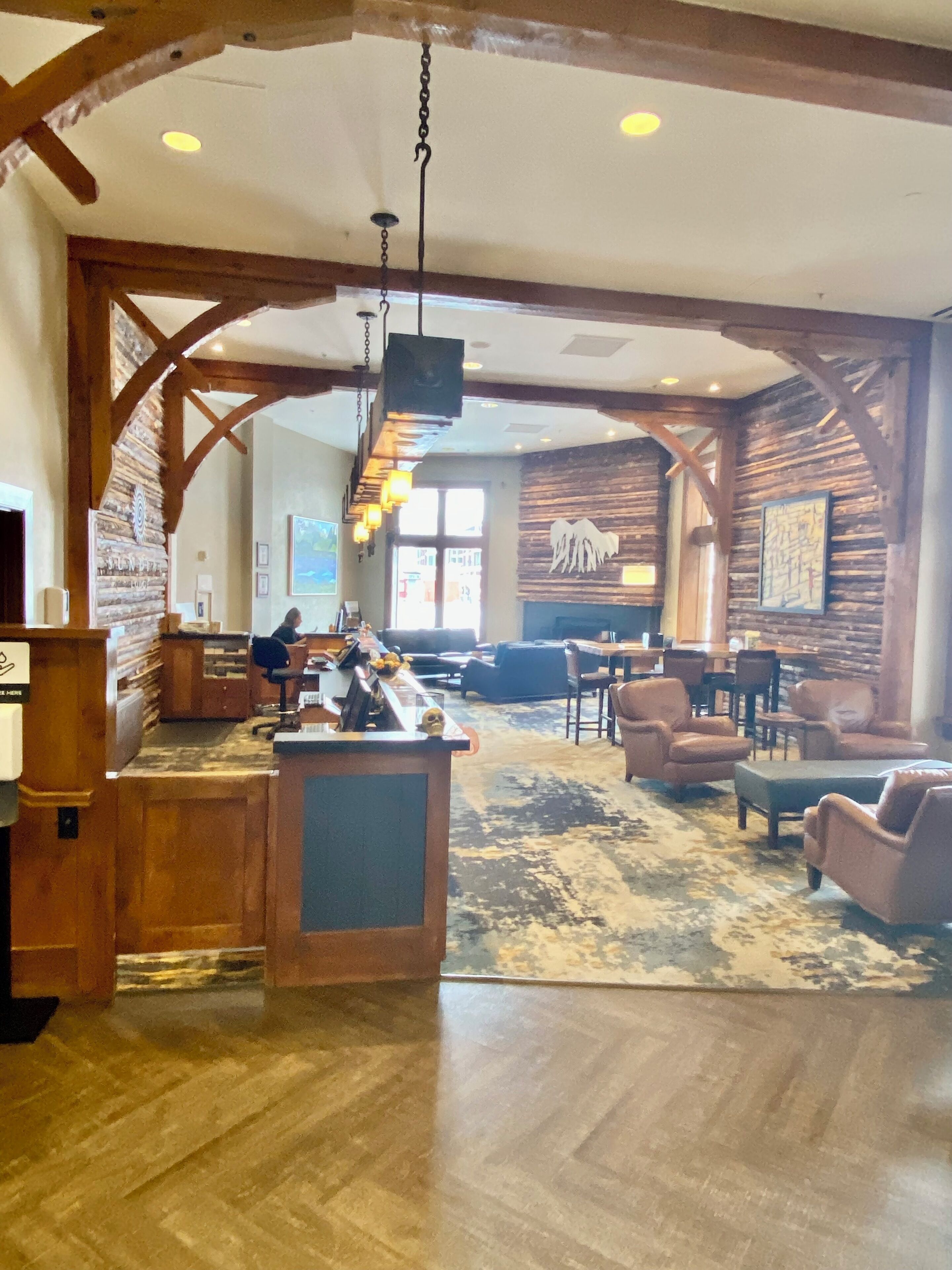 A spacious lobby with wooden beams, a reception desk, comfortable seating, and a large window providing natural light.