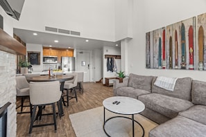 A modern living room with a grey sofa, a coffee table, and a dining area with a round table and chairs.