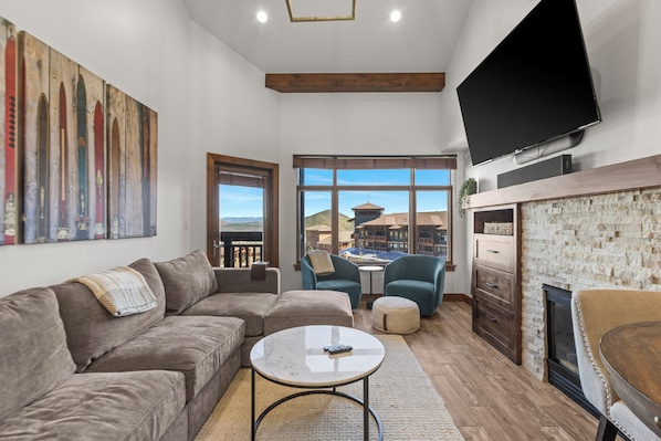 A modern living room with a sectional sofa, a coffee table, and a flat-screen TV mounted on the wall.