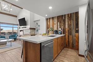 A modern kitchen with a large island, wooden accents, and a flat-screen TV mounted on the wall.