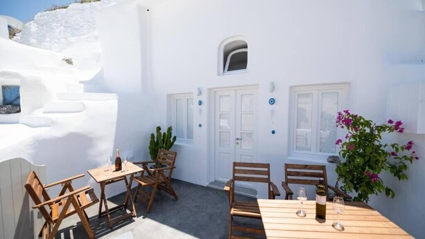 A white building with a wooden table and chairs, a potted plant, and a door with a window.