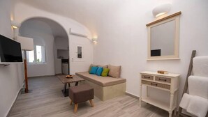 A modern, well-lit room with a sofa, a small table, a bench, a vanity with drawers, a mirror, and a television.