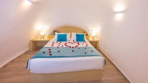 A neatly made bed with a blue and white bedspread, two blue pillows, and a heart-shaped arrangement of red rose petals on the bed.