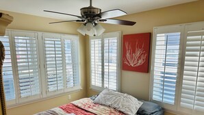 Ein Schlafzimmer mit einem Bett, einem Deckenventilator und Fenstern mit Jalousien.