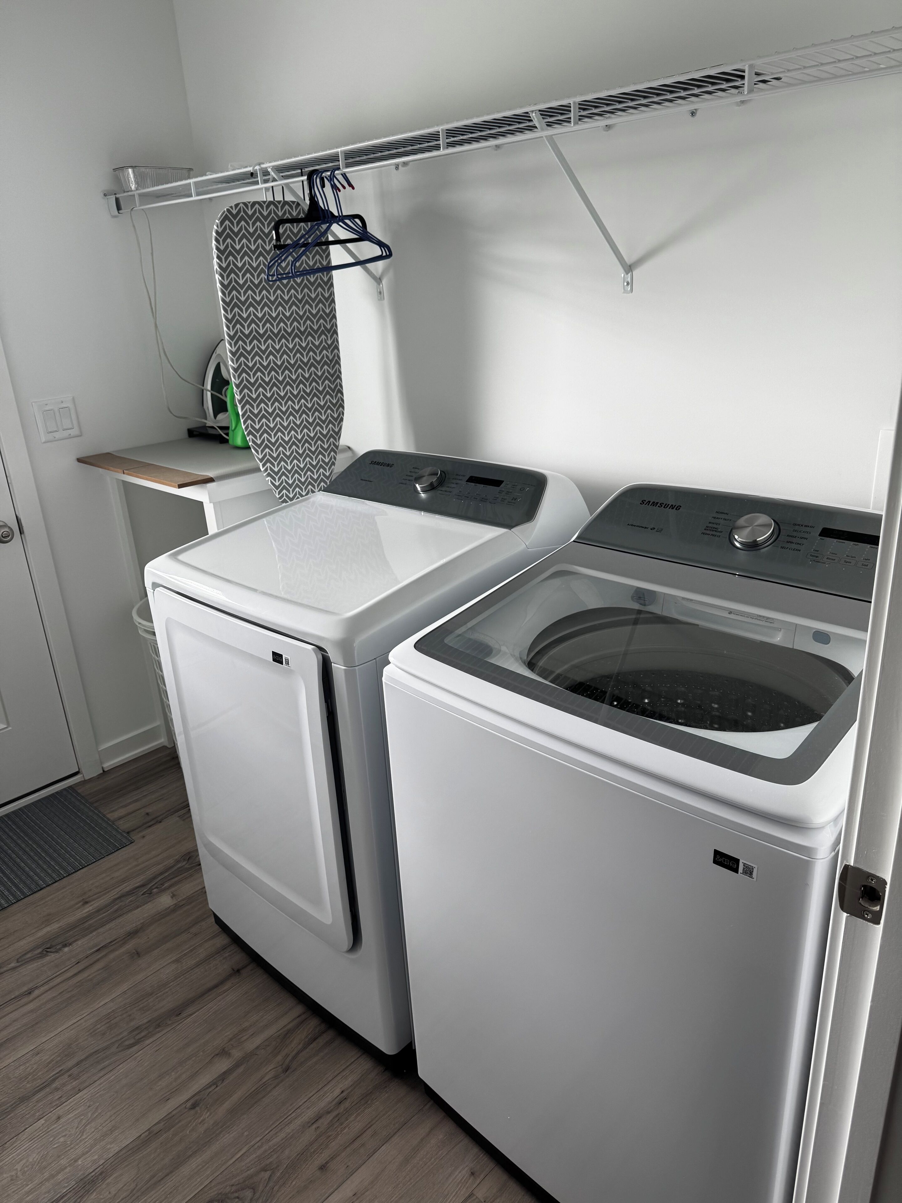 Een praktische wasruimte met een voorlader wasmachine en droger, een droogrek en een klein plankje met een mand.