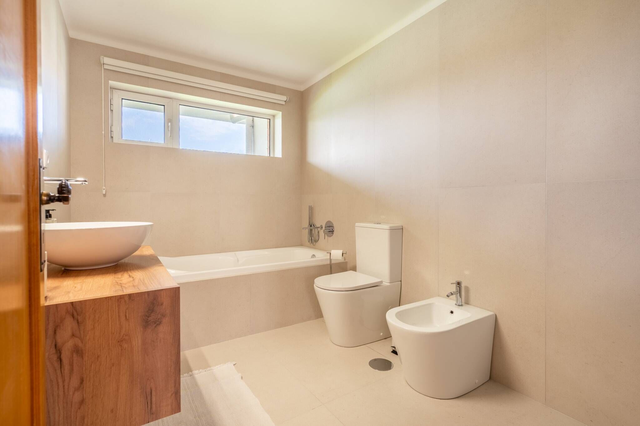 Een moderne badkamer met een groot bad, toilet, bidet en een houten wastafelmeubel.